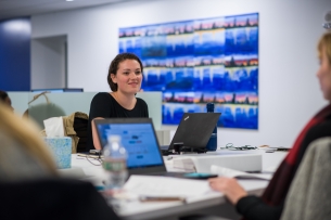 Young woman smiles and looks up from her laptop at a colleague in a shared office space. 